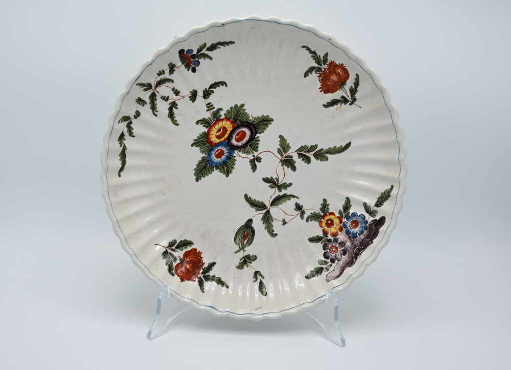 An 18th century Italian maiolica plate, attributed to the Antonibon manufactory in Nove di Bassano. The plate is shaped with a finely moulded. Painted with flowering plants issuing from rockwork and scattered sprays, blue-edged rim. This type of decoration is referred to as 'a blanser' in the factory inventory records and more recently by as 'tacchiolo' in some ceramics literature. Related Literature: G. Ericani et al., La ceramica degli Antonibon, exhibition catalogue, Milan 1990. Diameter: 28 cm. Condition: Very good condition; minor wear consistent with age.