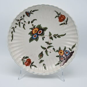 An 18th century Italian maiolica plate, attributed to the Antonibon manufactory in Nove di Bassano. The plate is shaped with a finely moulded. Painted with flowering plants issuing from rockwork and scattered sprays, blue-edged rim. This type of decoration is referred to as 'a blanser' in the factory inventory records and more recently by as 'tacchiolo' in some ceramics literature. Related Literature: G. Ericani et al., La ceramica degli Antonibon, exhibition catalogue, Milan 1990. Diameter: 28 cm. Condition: Very good condition; minor wear consistent with age.