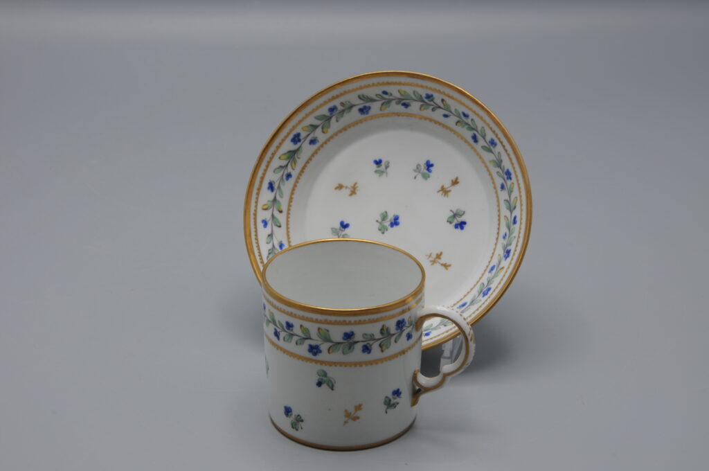 Cup and saucer in the style of Chantilly porcelain, bearing faux Chantilly marks, attributed to the Samson manufactory, Paris, 19th century. The decoration is hand-painted in the "Décor Barbeaux" pattern, consisting of scattered cornflowers (Centaurea cyanus) and other botanical elements. The Barbeaux décor was originally developed by the Sèvres Manufactory in the late 18th century for Marie Antoinette, reflecting a preference for naturalistic floral designs associated with the Queen’s taste. This style was used primarily on hard-paste porcelain produced at Sèvres beginning in the 1780s. The form and decoration of the cup and saucer closely follow the late 18th-century models, with gilded accents applied to the rim and handle. The cup stands 6 cm high; diameter 5,5 cm (ex the ear) . Both pieces exhibit signs of wear consistent with age. Pseudo mark Chantilly Samson - Porcelain Cup and Saucer decor 'Aux Barbeaux' - late19th century French