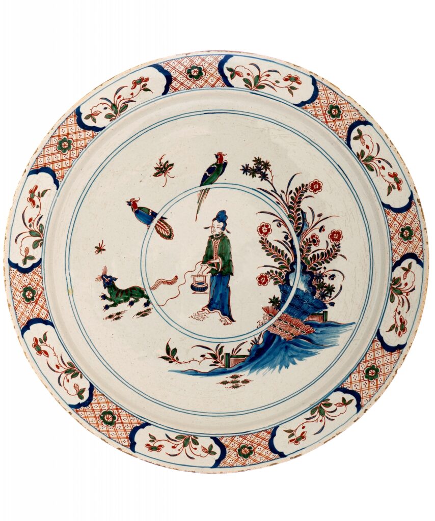 An exceptionally large Dutch Delftware charger decorated in the Cashmere palette of cobalt blue, green and iron red. The central scene depicts an Oriental figure in a stylised garden, accompanied by a striking green panther. Flowering plants and ornamental rockwork complete the chinoiserie composition.